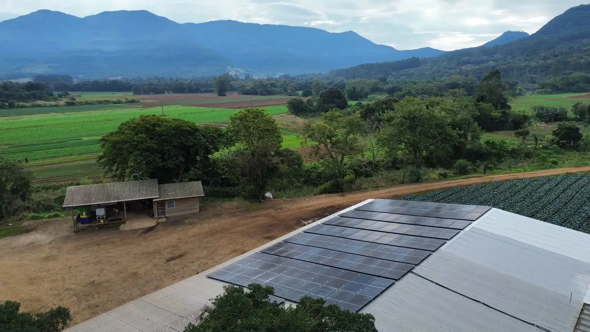Galpão rural com módulos fotovoltaicos no telhado e lavouras ao fundo