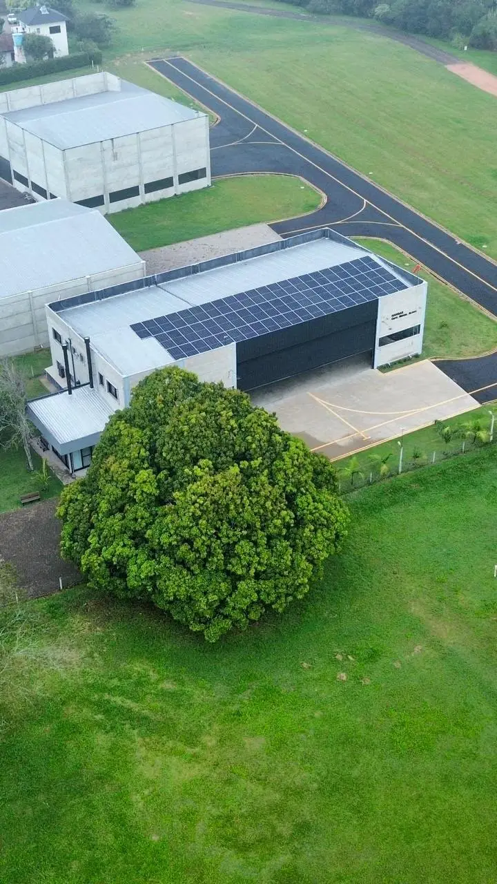 Galpão com módulos fotovoltaicos e pátio gramado, vista aérea