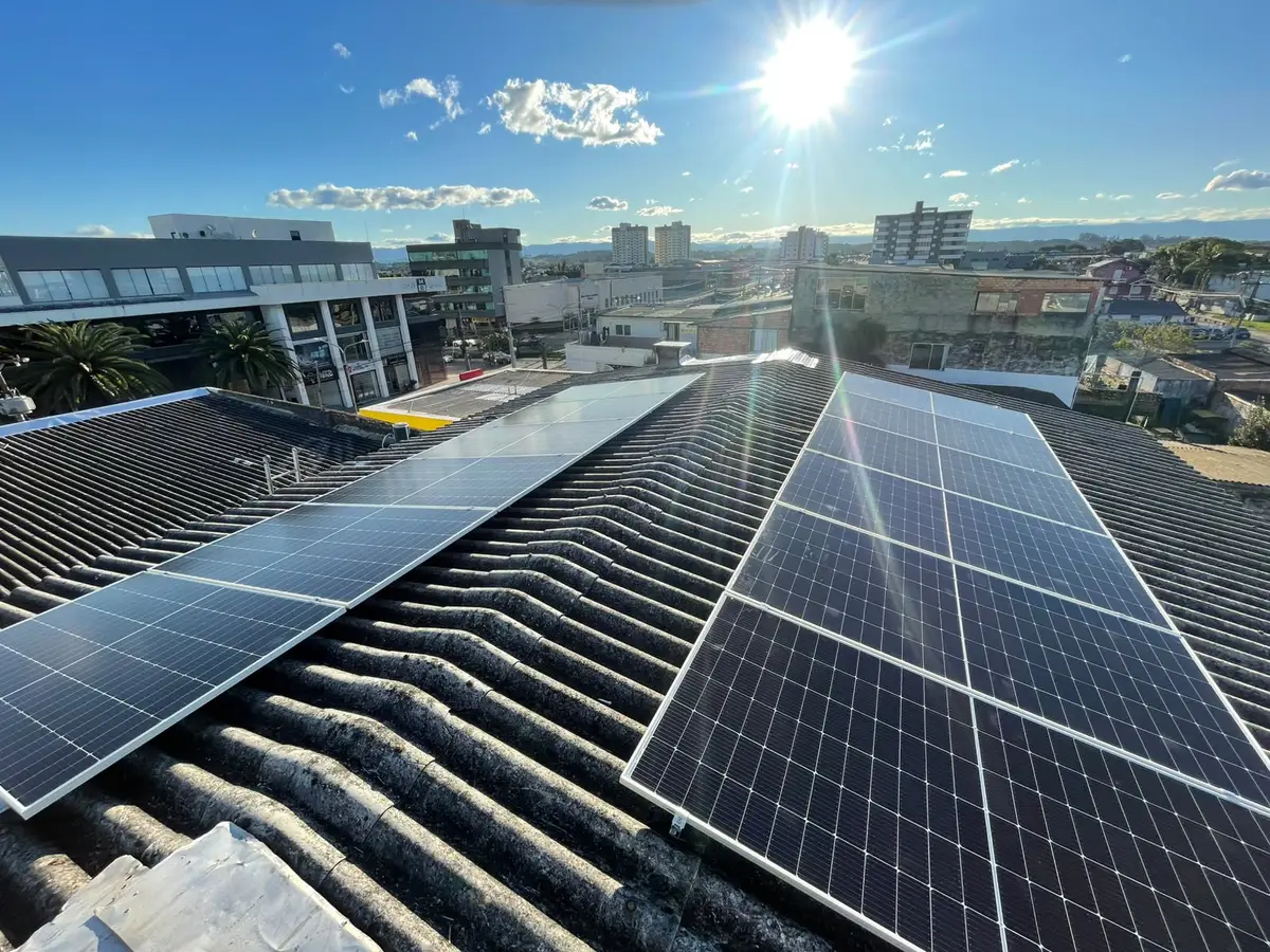 Módulos fotovoltaicos em telhado de fibrocimento, com a cidade ao fundo